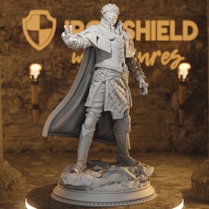 May include: A gray 3D printed figurine of a person wearing a cloak and armor, standing on a rocky base. The figurine is posed with one hand raised and the other holding a sword. The background is a blurry image of a brick wall.