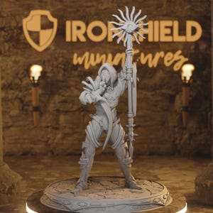 Può includere: Una miniatura grigia di un personaggio incappucciato che tiene in mano un bastone con un disegno a forma di occhio. La figura è in piedi su una base circolare con dettagli intricati. Lo sfondo presenta il testo "IRONSHIELD miniatures".
