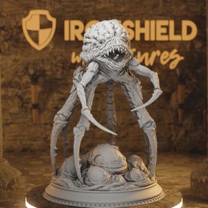 Op de afbeelding: Een grijze, gedetailleerde, 3D-geprinte miniatuur van een monsterlijk wezen met meerdere poten en een groot hoofd. Het wezen staat op een basis met verschillende kleinere, ronde objecten. De miniatuur is gelabeld met "IRONSHEILD miniatures".