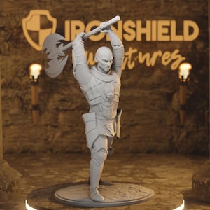 May include: A grey figurine of a warrior raising an axe overhead. The figure is clad in armour with a lion emblem on the chest. The background features the text "IRONSHIELD" and "ventures". The figurine is on a circular base.