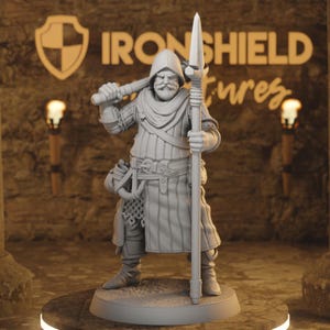Könnte beinhalten: Graue Figur eines mittelalterlichen Kriegers, der einen Speer und eine Keule hält. Der Krieger trägt eine Kapuzen-Tunika und hat einen Schnurrbart und Bart. Der Text "IRON SHIELD" ist im Hintergrund sichtbar.