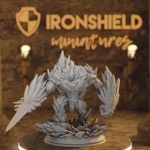 Op de afbeelding: Een grijze miniatuurfiguur van een stenen golem met een schild en een zwaard. De figuur staat op een basis van grillige rotsen. De tekst "IRONSHIELD miniatures" is zichtbaar op de achtergrond.