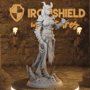 Può includere: Figurina grigia dettagliata di una guerriera con corna, armatura e frusta. La figura è su una base con teschi. Il logo Iron Shield è visibile sullo sfondo.