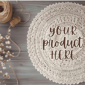 May include: A white crocheted doily with the text "your product here" on a wooden surface with dried flowers and twine.