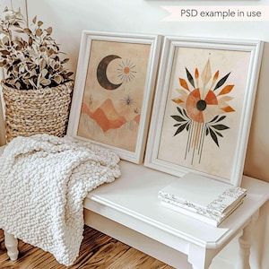 Puede incluir: Dos impresiones enmarcadas con diseños abstractos en tonos naranja, marrón y negro. Las impresiones están colgadas en una pared blanca sobre un banco blanco con una manta blanca y una pila de libros.