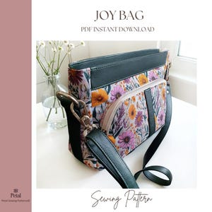 May include: A floral print shoulder bag with a black strap and accents. The bag features a zippered front pocket and the text "JOY BAG PDF INSTANT DOWNLOAD" at the top. The words "Sewing Pattern" are at the bottom.