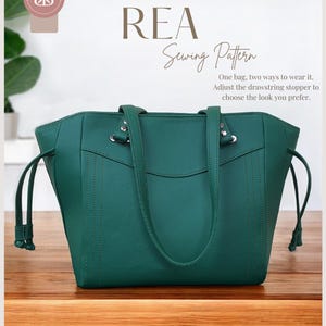 May include: A green tote bag with two straps and a drawstring closure. The bag has a simple design with stitching details. The text "REA Sewing Pattern" is above the bag. The text below the bag reads "One bag, two ways to wear it. Adjust the drawstring stopper to choose the look you prefer."