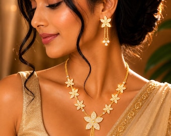 May include: A gold-toned necklace and matching earring set featuring a floral motif. The necklace consists of several small flower charms connected by a chain, with a larger central flower pendant that has three dangling teardrop-shaped accents.