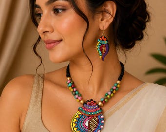 May include: A handcrafted jewellery set featuring a necklace and matching earrings. The necklace has a black cord with multi-coloured beads and a large, hand-painted pendant. The pendant and earrings display intricate patterns in yellow, blue, pink, and orange.