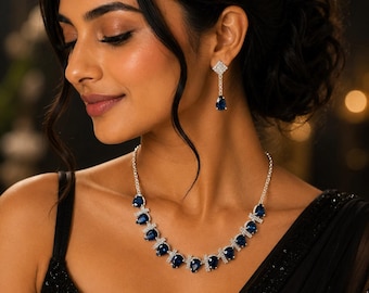 May include: A silver-toned necklace and matching drop earring set featuring pear-shaped deep blue stones surrounded by small clear crystals. The necklace has a linked chain design, and the earrings feature a square stud with a dangling blue stone.