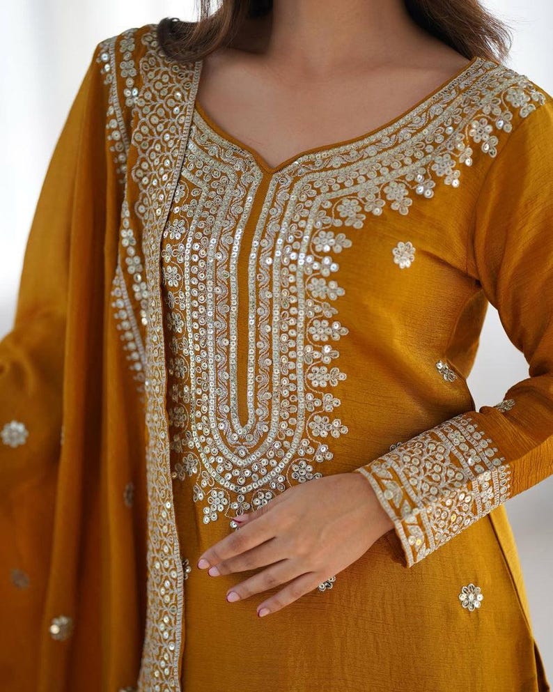 May include: A mustard yellow long-sleeved tunic featuring an intricate silver sequin and thread embroidery pattern around the neckline, cuffs, and along the edge of the matching draped shawl, creating a detailed metallic floral design.