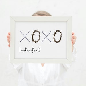 May include: White framed print with the word "XOXO" in black text. The "O"s are replaced with a crown of thorns. The text "Love shown for all" is below the word "XOXO".