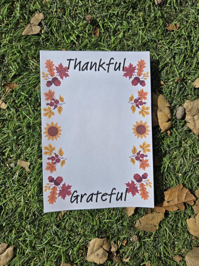 May include: A white card with a fall-themed border featuring sunflowers, leaves, and berries. The card says "Thankful" at the top and "Grateful" at the bottom.