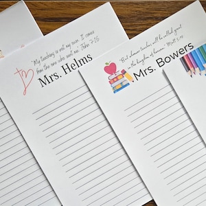 May include: Four lined notepads with different teacher-themed designs. The top notepad has a pencil and the text "Teacher Notes". The second notepad has a red heart and the text "My teaching is not my own. I came from the one who sent me. John 7:16 Mrs. Helms". The third notepad has a stack of books, an apple, and a pencil with the text "But a true teacher will be called great in the kingdom of heaven. Matt 5:19 Mrs. Bowers". The fourth notepad has a row of colored pencils with the text "Ms. Browmell".