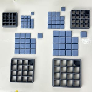 May include: A set of eight grey plastic square tile moulds, some with blue square tiles inside. The moulds are different sizes and are arranged on a white surface. The text "801" is in the bottom right corner of the image.
