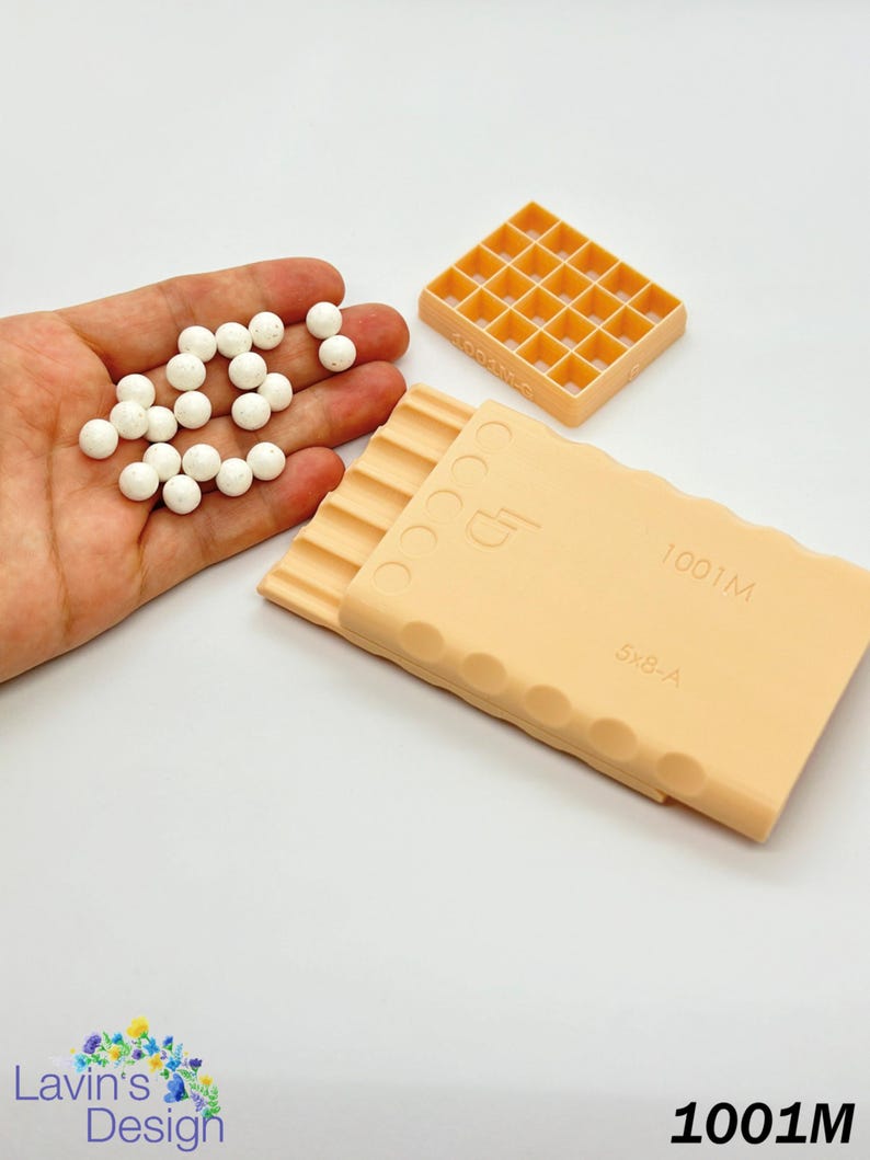 May include: A set of two peach-colored plastic molds for making candy or chocolate. The larger mold has a grid pattern with 20 squares. The smaller mold has a series of ridges and the text "1001M 5x8-A". A hand is holding 20 white round candy pieces.