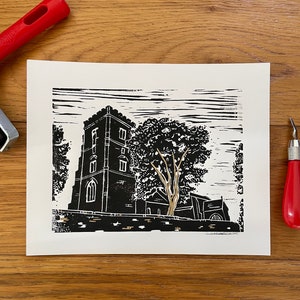 Puede incluir: Grabado en linóleo en blanco y negro de un edificio de iglesia con una torre alta y un árbol en primer plano. La impresión es en papel blanco y tiene un aspecto texturizado.