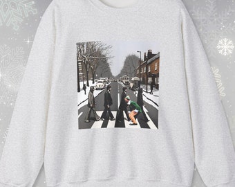 May include: A grey sweatshirt featuring a printed image of the Beatles crossing Abbey Road in a snowy setting. The image is in black and white, except for the Beatles, who are in colour.