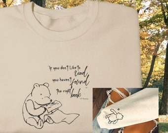 Op de afbeelding: Een crèmekleurige trui met een zwarte illustratie van Winnie de Poeh die een boek leest. De quote "Als je niet graag leest, heb je het juiste boek nog niet gevonden." staat op de trui gedrukt.