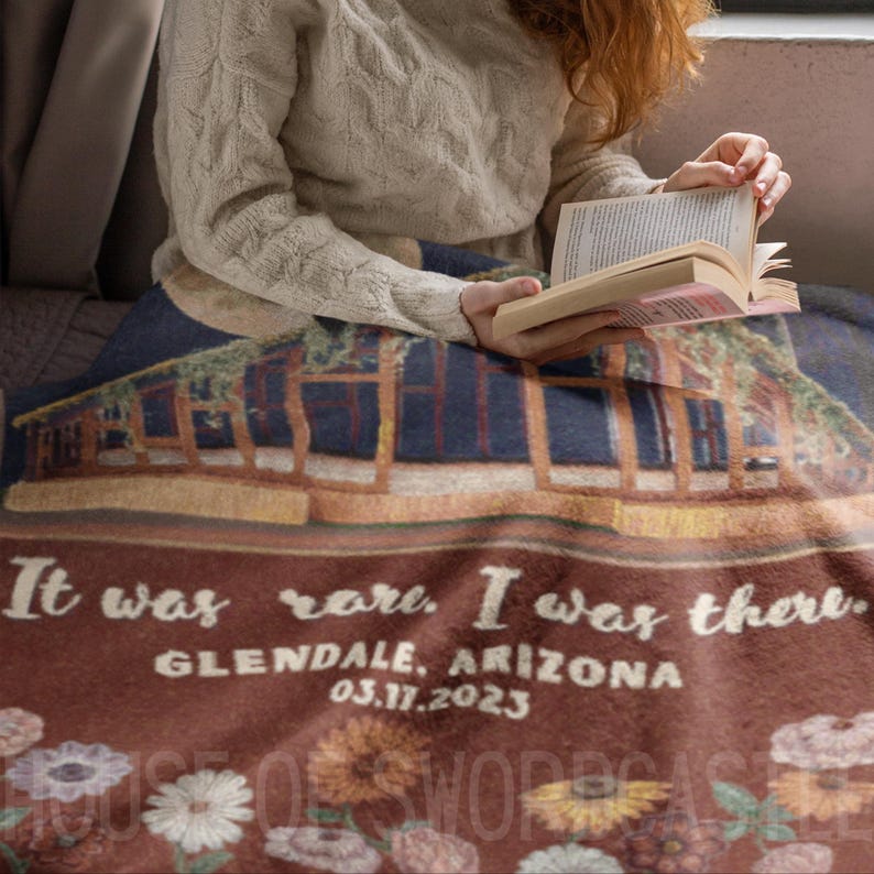 Op de afbeelding: Een bruin en cr&egrave;mekleurig fleece deken met een bloemenpatroon en de tekst "It was rare. I was there. Glendale, Arizona 03.11.2023"