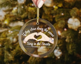May include: A clear glass Christmas bauble with the text "If they close down the venue Sing in the Streets - Vienna 2024" and a cartoon image of two hands forming a heart shape.