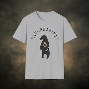May include: A gray t-shirt with a black bear holding a gold ring with a diamond. The text "RINGBEAR(ER)" is printed in black around the bear.