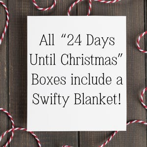 May include: A white square card with black text that reads "All '24 Days Until Christmas' Boxes include a Swifty Blanket!" is surrounded by red and white twine on a dark wood background.
