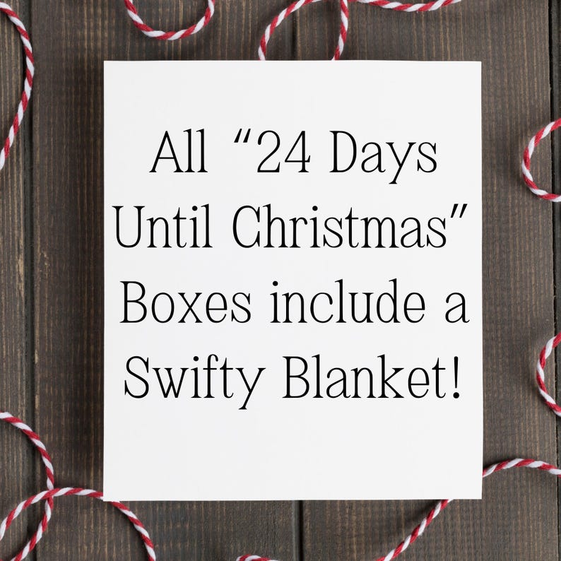 May include: A white square card with black text that reads "All '24 Days Until Christmas' Boxes include a Swifty Blanket!" is surrounded by red and white twine on a dark wood background.