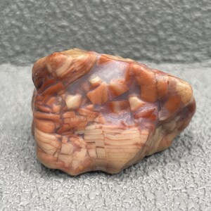 May include: A natural stone with a mix of colors, including shades of orange, brown, and cream. The stone has a rough, textured surface with a unique pattern of lines and shapes. The stone is a decorative item.