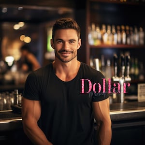 May include: A man wearing a black scoop-neck t-shirt smiles at the camera. The text "Dollar Mockup Shop" is visible on the shirt. The background is a blurred bar setting with bottles and taps.