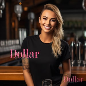 May include: A black crew neck t-shirt with the text "Dollar Mockup Shop" in pink glitter. The person in the image is smiling and has blonde hair. The background is a bar setting with a wooden bar and metal fixtures.