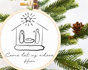 May include: A white fabric ornament with a black line drawing of the nativity scene and the text "Come let us adore Him".