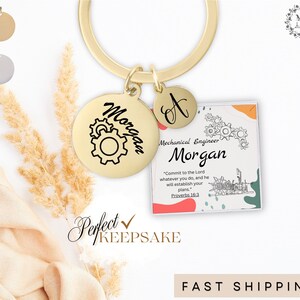 May include: Gold keychain with a round charm engraved with the name "Morgan" and a gear design. A smaller charm with the letter "A" is attached. A square charm with a mechanical engineering design and the text "Mechanical Engineer Morgan" and a Bible verse is also attached.
