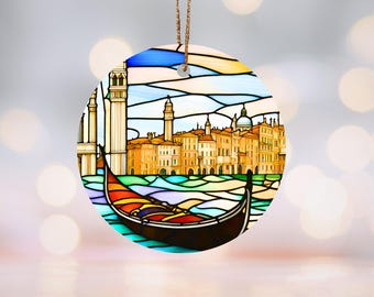 May include: A round, colorful stained glass ornament featuring a gondola floating in front of a cityscape. The cityscape is made up of buildings with domes and towers, and the sky is blue with white clouds.