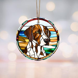 May include: Circular ornament with a stained-glass effect depicting a dog's head. The dog has brown and white fur, a black nose, and brown eyes. The ornament is framed by a colourful border and has a gold hanging string.