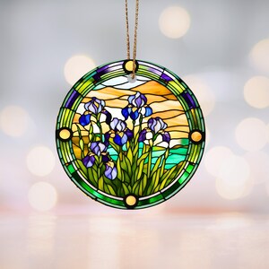 May include: Round stained glass ornament featuring a colorful depiction of iris flowers in shades of purple, green, and yellow. The ornament has a gold-colored border and a brown string for hanging.