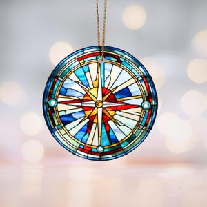 May include: A stained glass ornament featuring a compass rose with a red, blue, and yellow design. The compass rose is surrounded by a blue and white wave pattern.