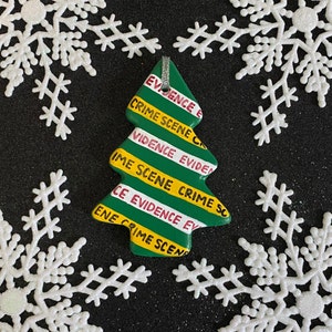 May include: A green Christmas tree ornament with yellow and red stripes that reads "EVIDENCE E CRIME SCENE CRIME SC CE EVIDENCE EV ENE CRIME SCENE".