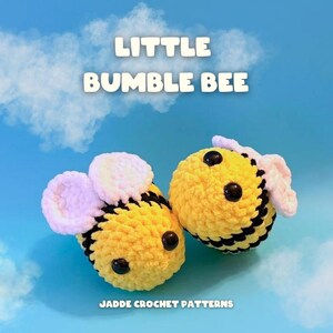 May include: Two small, round, crocheted bumble bee plushies with yellow and black horizontal stripes, black plastic eyes, and light pink wings. The text 'LITTLE BUMBLE BEE' and 'JADDE CROCHET PATTERNS' is visible against a blue sky background.