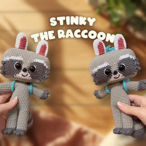 May include: Two crocheted raccoon dolls with grey bodies, dark grey eye patches, and white accents. Each doll features large black eyes, a small black nose, a stitched smile, pink-lined ears, and a light blue backpack. The text reads STINKY THE RACCOON.