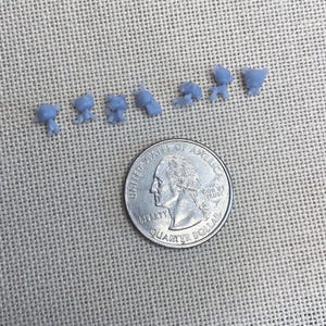 Puede incluir: Siete figuras de animales en miniatura de color azul claro dispuestas en una fila horizontal sobre una moneda de 25 centavos de dólar estadounidense. Las pequeñas figuras tienen formas y orejas distintas, mostrando la escala frente a la moneda de 2,43 cm.