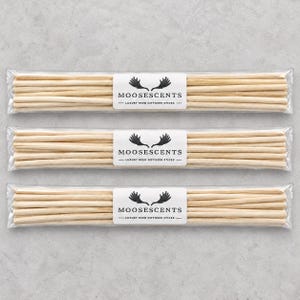 May include: Three clear plastic packages, each containing a bundle of light-colored wooden reed diffuser sticks. A white rectangular label on each package features a black moose antler logo and the text MOOSESCENTS LUXURY REED DIFFUSER STICKS.