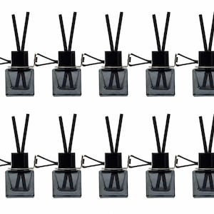 May include: A collection of twelve car air fresheners. Each freshener features a small, square, gray glass bottle with black reeds and a black cap. A silver clip is attached for easy placement in a car vent.