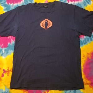 Puede incluir: Una camiseta azul marino con un logotipo de Cobra rojo de la serie de dibujos animados G.I. Joe.