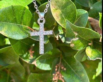 May include: A silver chain necklace with a small, clear crystal cross pendant.