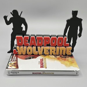 Peut inclure: Une figurine 3D de Deadpool et Wolverine posée sur un boîtier de disque Blu-ray pour le film "Deadpool & Wolverine". La figurine est noire et le texte est rouge et or.