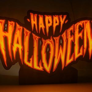 May include: A Halloween-themed illuminated sign. The words "HAPPY HALLOWEEN" are displayed in orange and yellow, with a jagged, spooky font. The sign is set against a dark background.