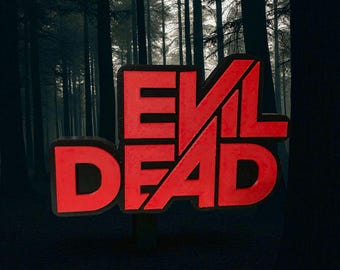 May include: A red "EVIL DEAD" sign with a black outline against a dark forest backdrop. The text is in a bold, stylized font, with the letters appearing three-dimensional. The background features tall, silhouetted trees.