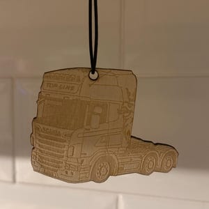 Peut inclure: Ornement en bois en forme de camion, avec les mots "TOP LINE" et "SCANIA" gravés. Suspendu par une ficelle noire, idéal pour la décoration.