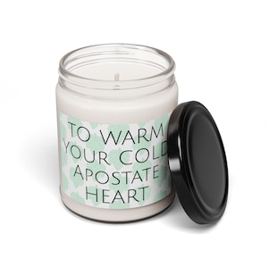 May include: A white candle with a black lid and a green and white label that reads "To warm your cold apostate heart".